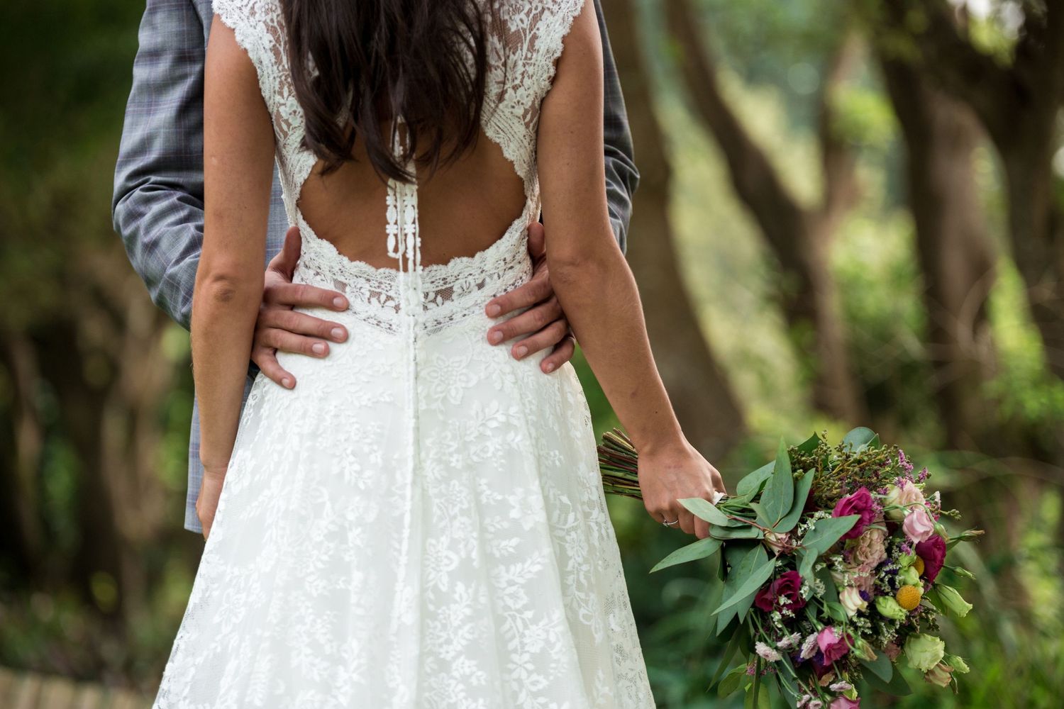 Elegant white lace wedding dresses displayed in an outdoor garden setting.