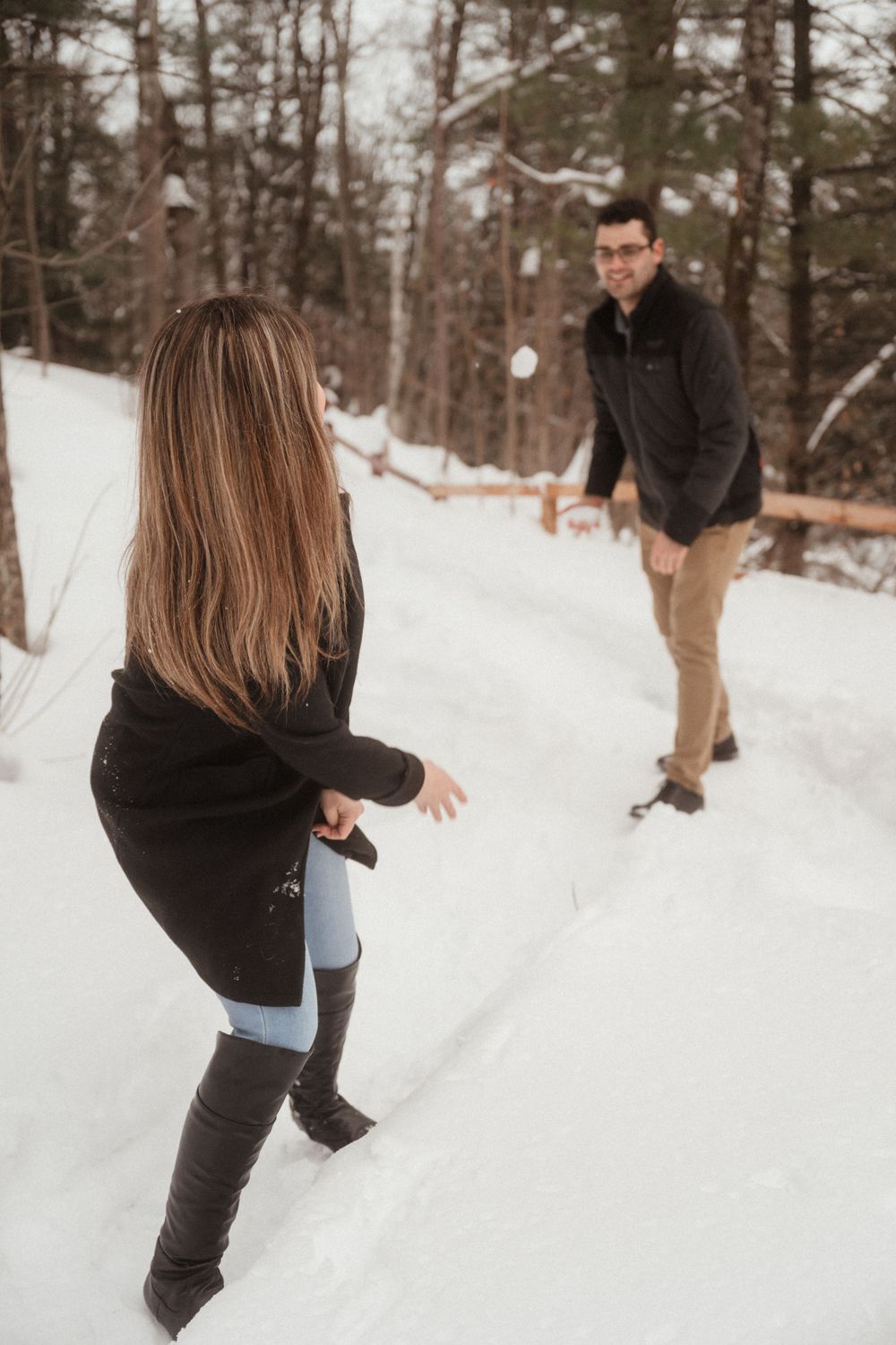 Couple having a playful snowball fight on a snowy trail surrounded by winter trees.