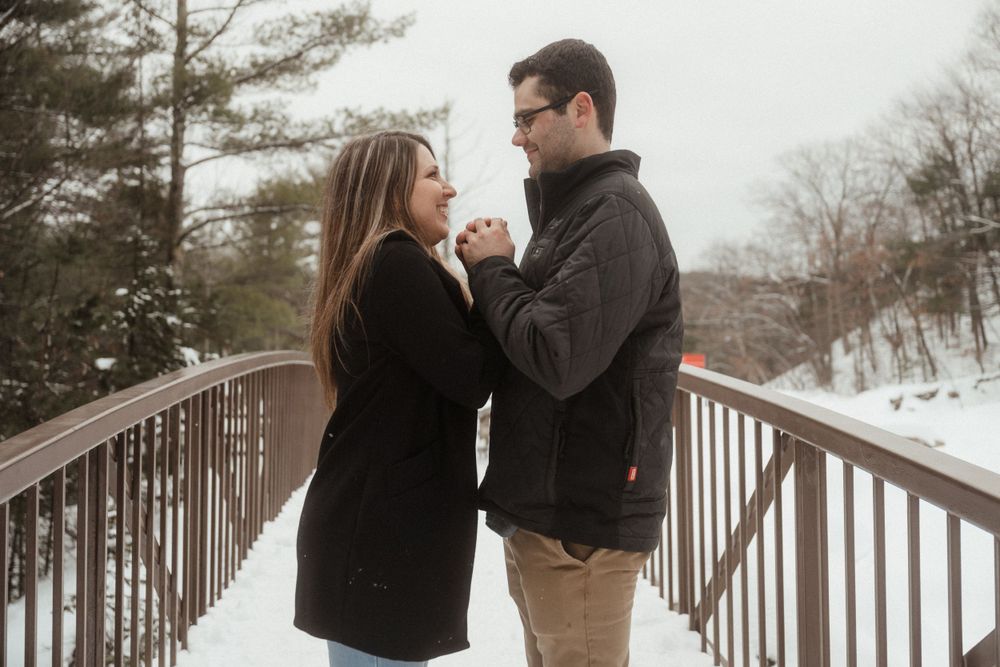 Romantic winter portrait of a couple holding hands on a snow-covered bridge.