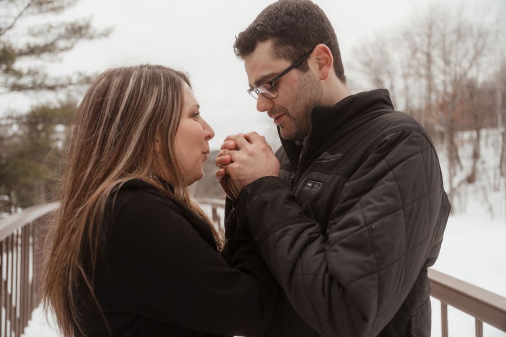 Intimate moment between a couple holding hands close on a snowy bridge in winter.