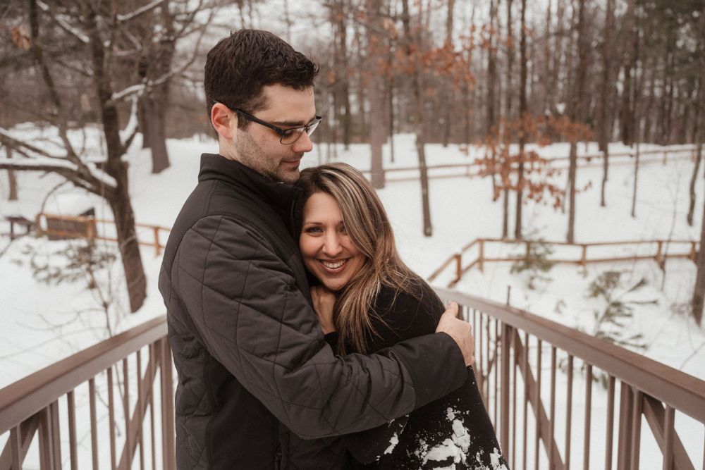 Couple sharing a warm embrace on a bridge during a snowy winter day.