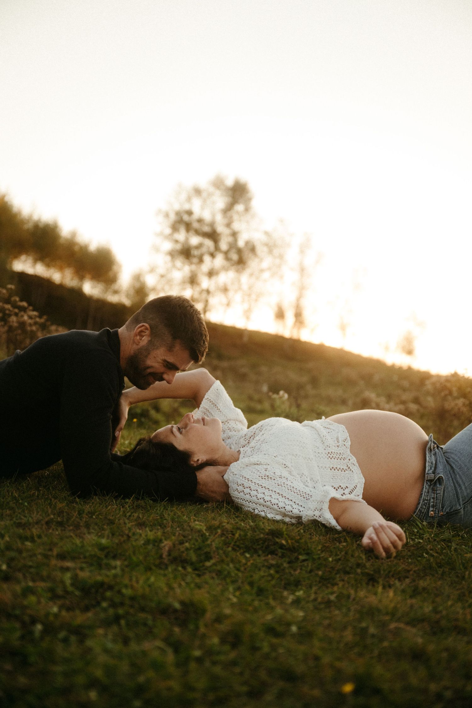 A couple shares an intimate moment on a grassy hill during golden hour sunset.
