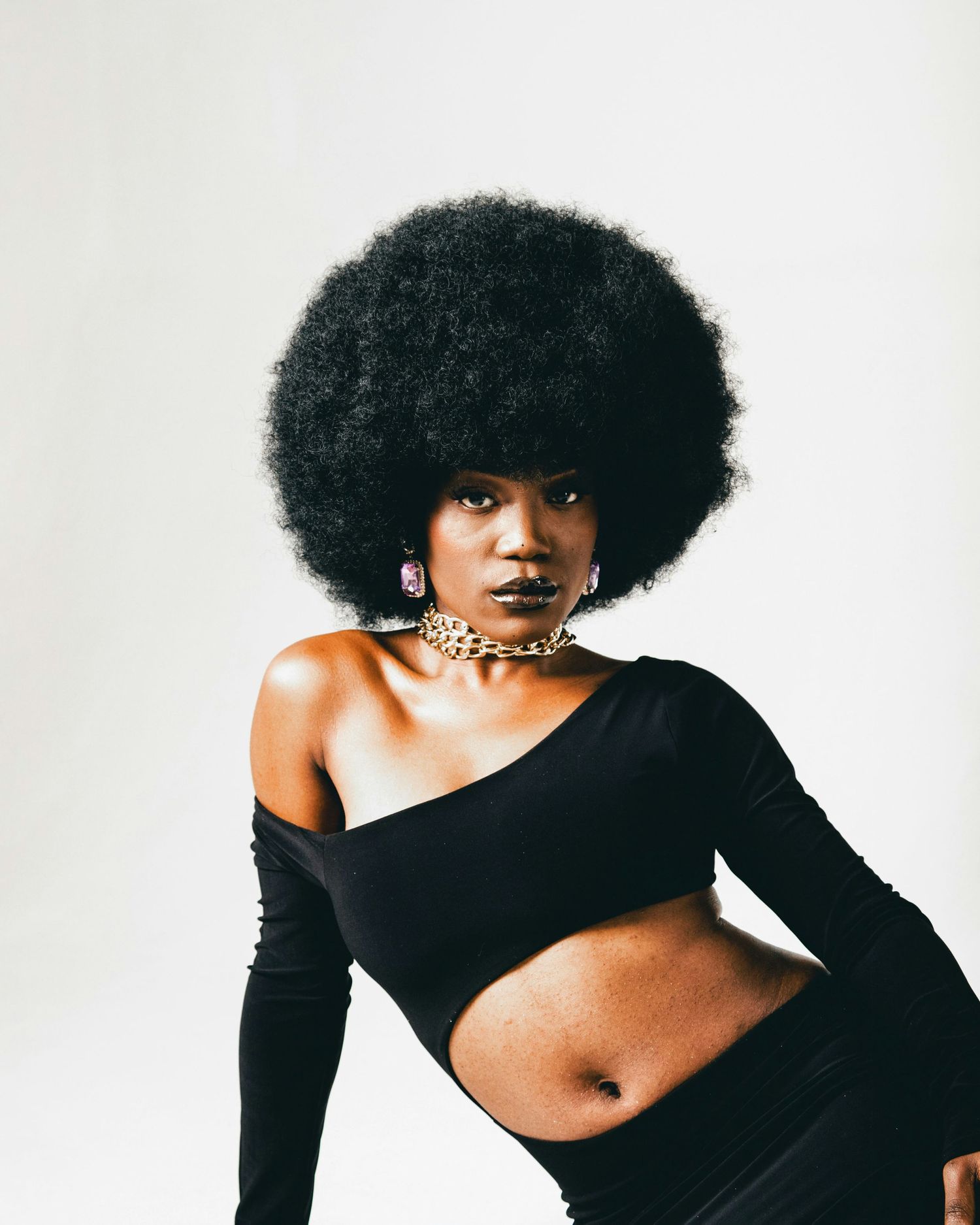 Fashion portrait of person with afro hairstyle wearing black asymmetric top and statement jewelry.