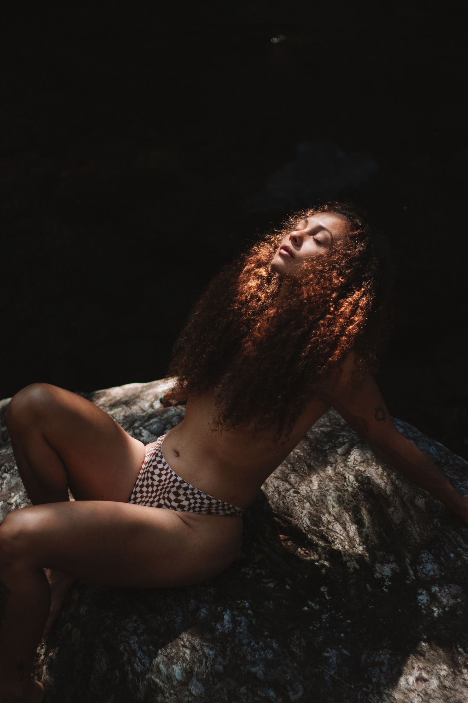 Model with curly hair seated on rock