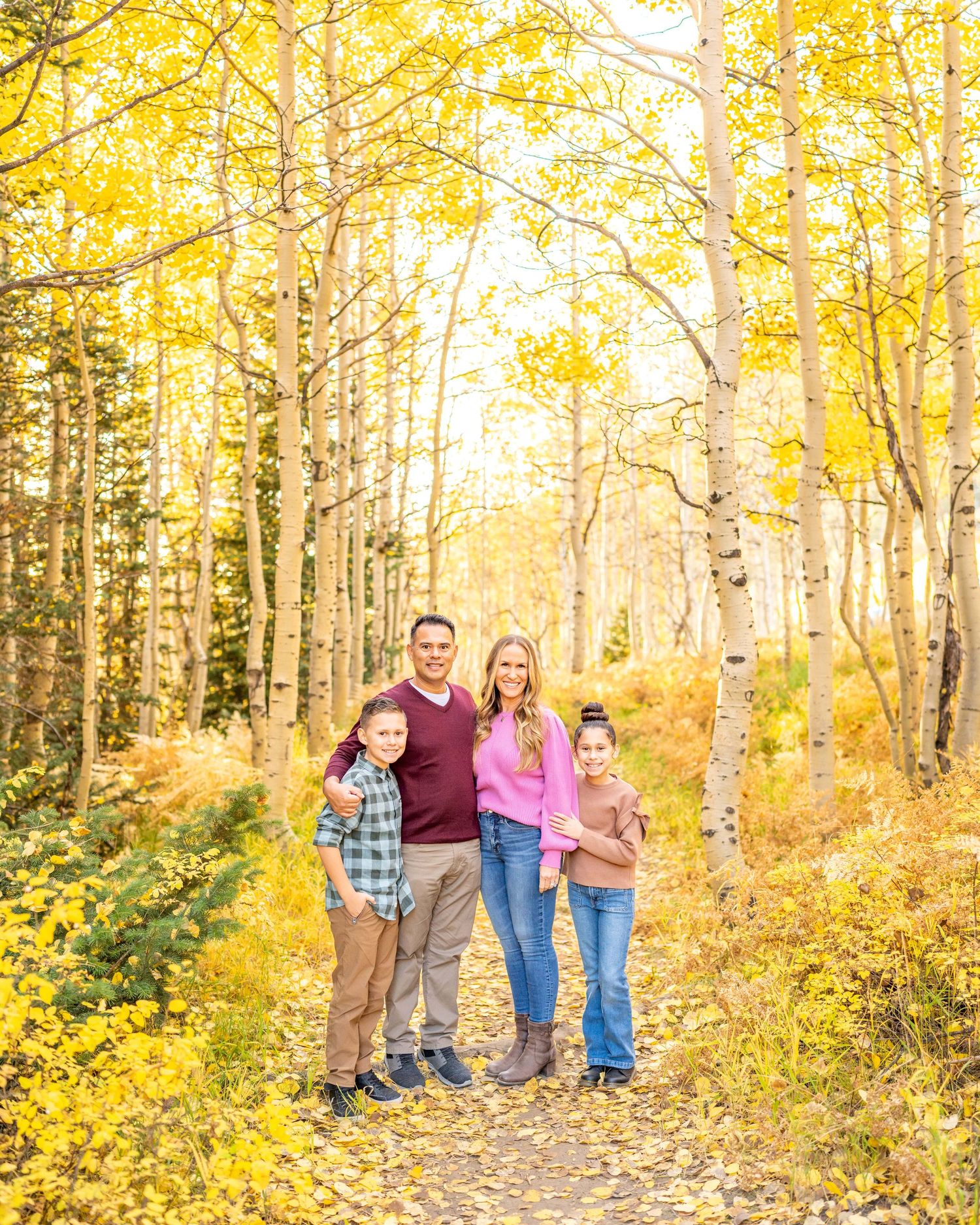 A family poses together on a forest trail surrounded by golden aspen trees in autumn at White Pines Trailhead.