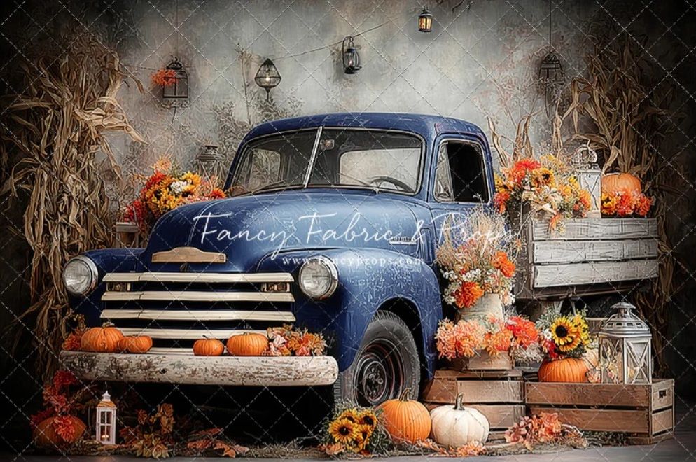 Vintage blue pickup truck decorated with fall pumpkins and autumn decorations in a rustic outdoor setting.