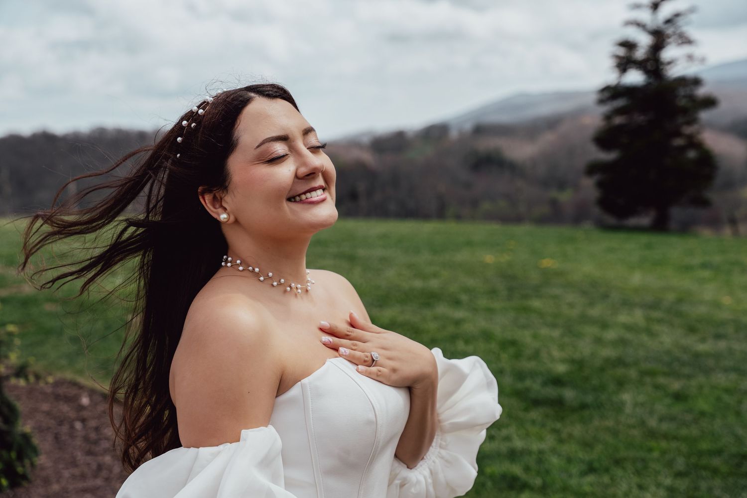 A joyful moment captured outdoors in a wedding dress with rolling green hills and mountains in the background.