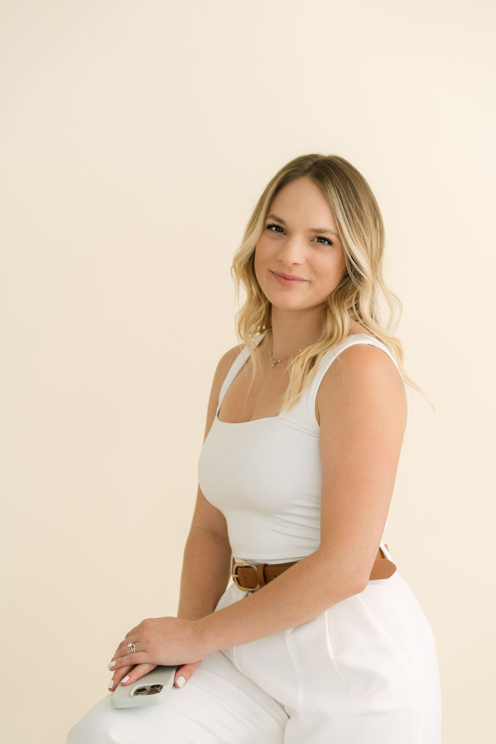 Casual portrait against beige background wearing white tank top.