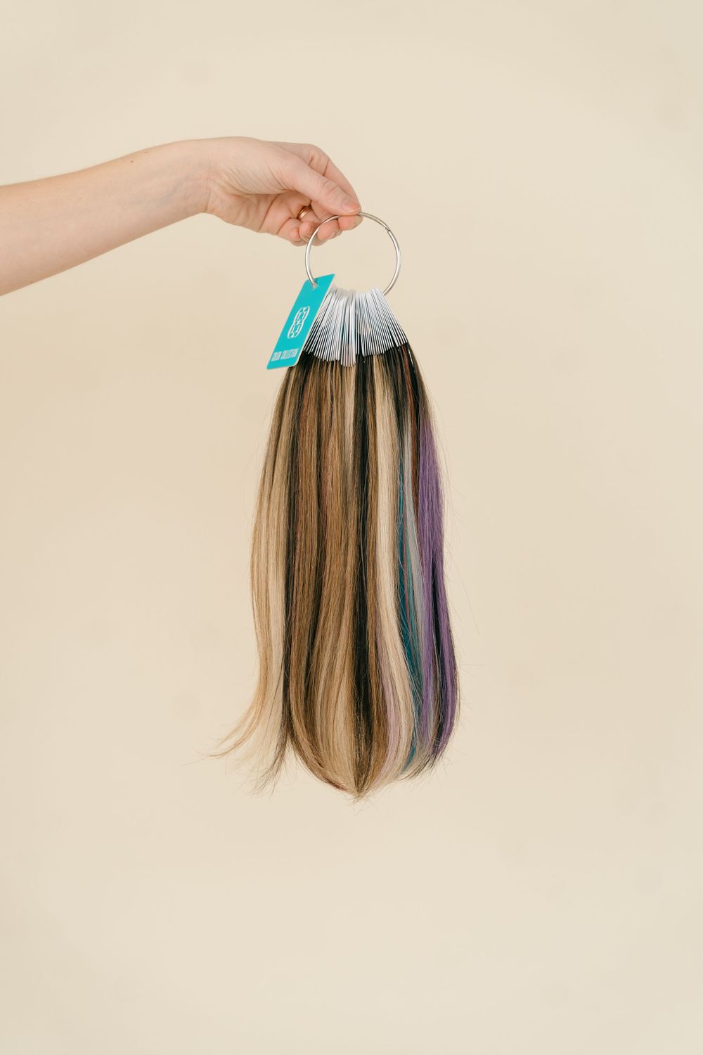Hand holding hair extension samples showing various colors and highlights.