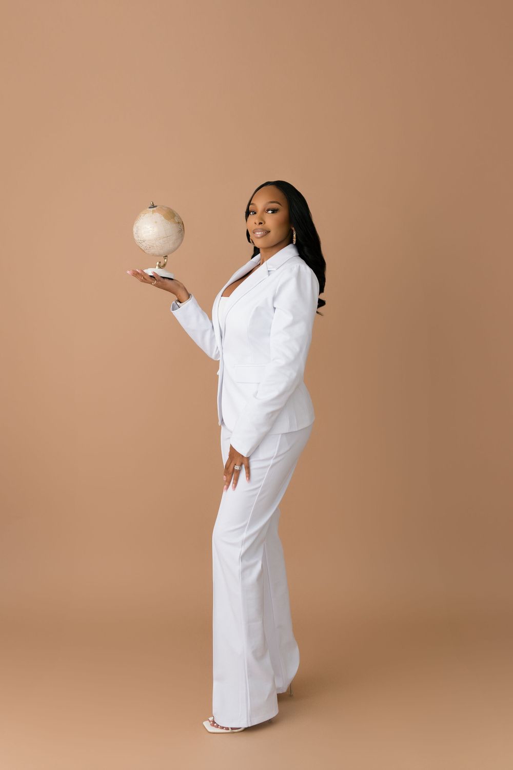 Professional in crisp white suit holds small globe against neutral background.