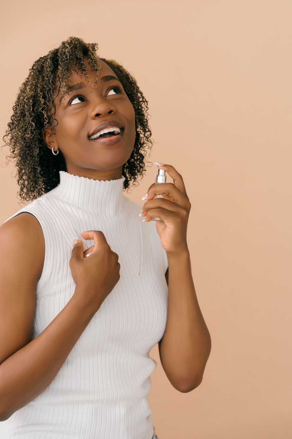 Person in white turtleneck sleeveless top expressing joy against beige background.