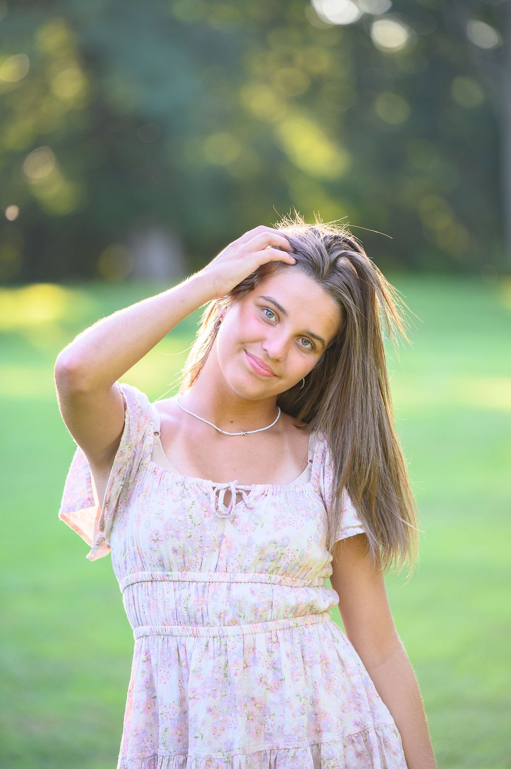 Summer portrait in a floral dress standing outdoors with sunlit bokeh background in the park.