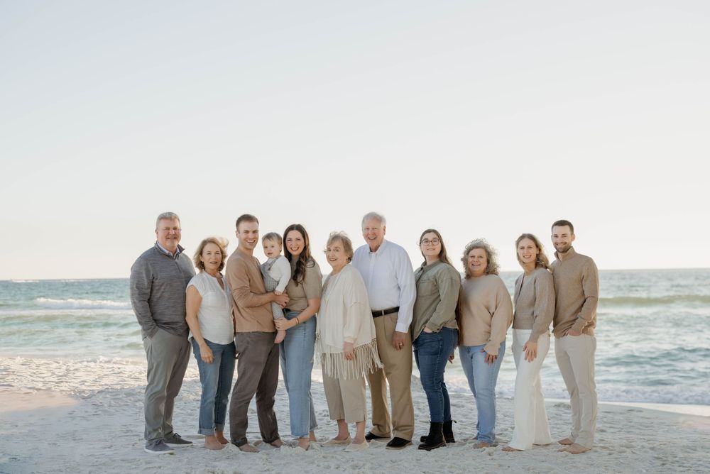 Group wearing coordinated neutral colored clothing poses together on a sunny beach with ocean waves in the background.