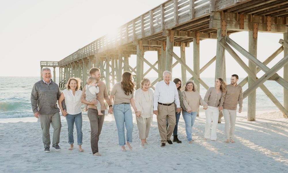 A group of people walking together along a beach pier during golden hour, casting long shadows on the sand.