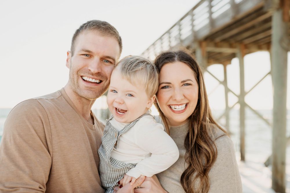 A happy family portrait captured outdoors with a wooden pier in the background.