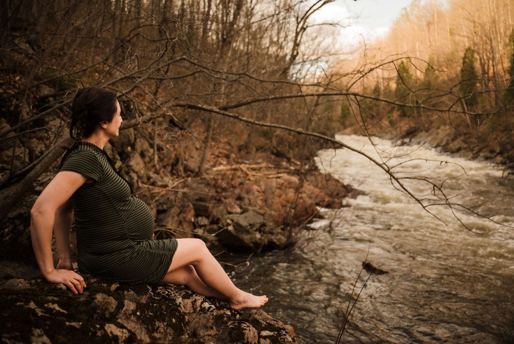 Maternity portrait by a rushing river surrounded by autumn foliage.