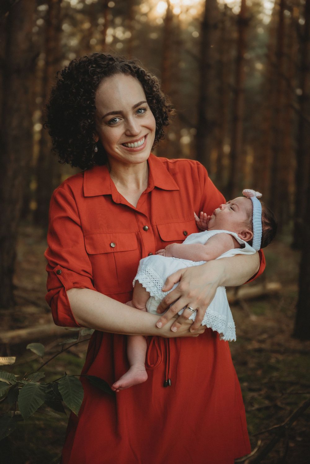 A tender moment captured in a forest setting with baby in white lace dress.