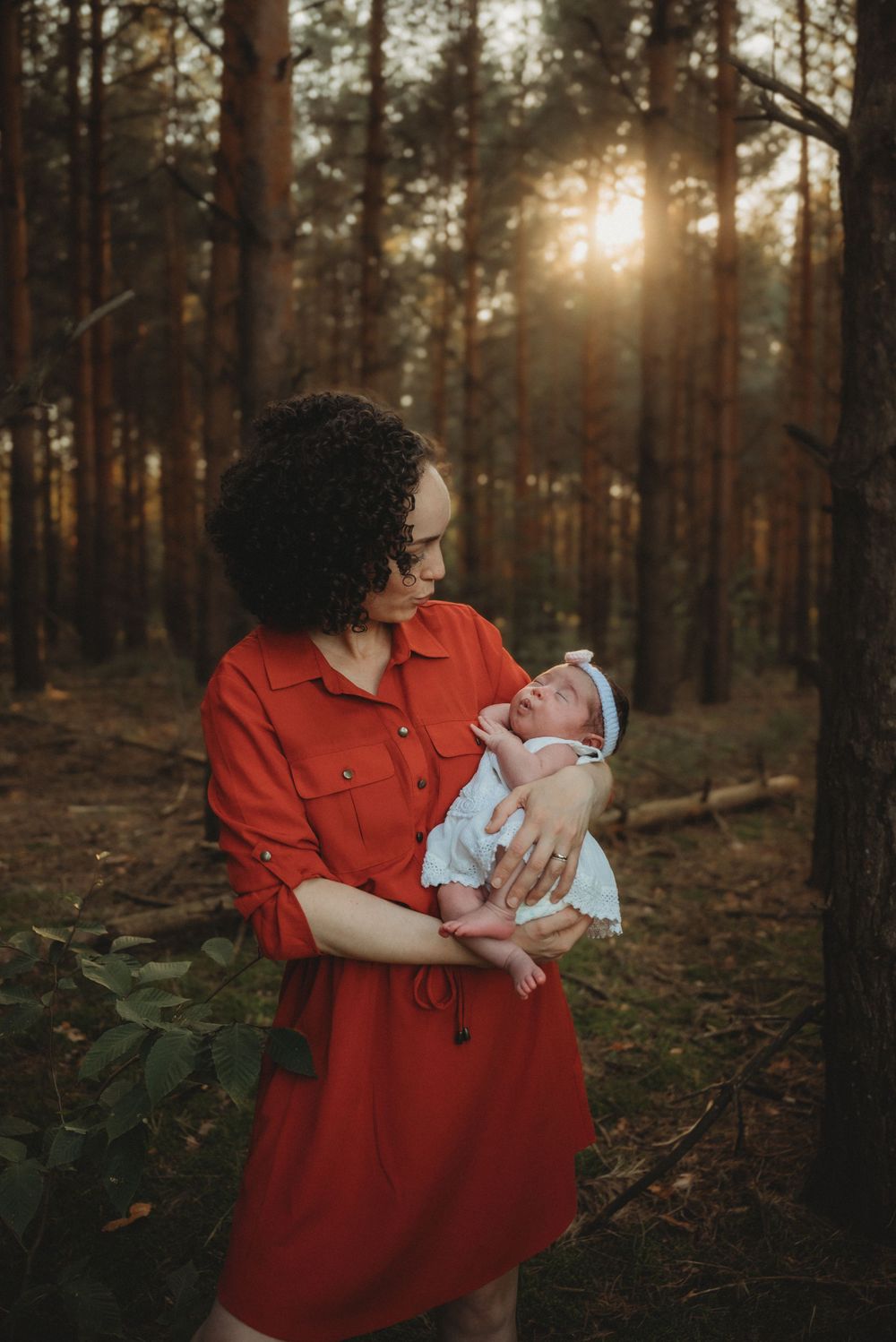 Sunset forest scene with baby in white dress against warm golden light.