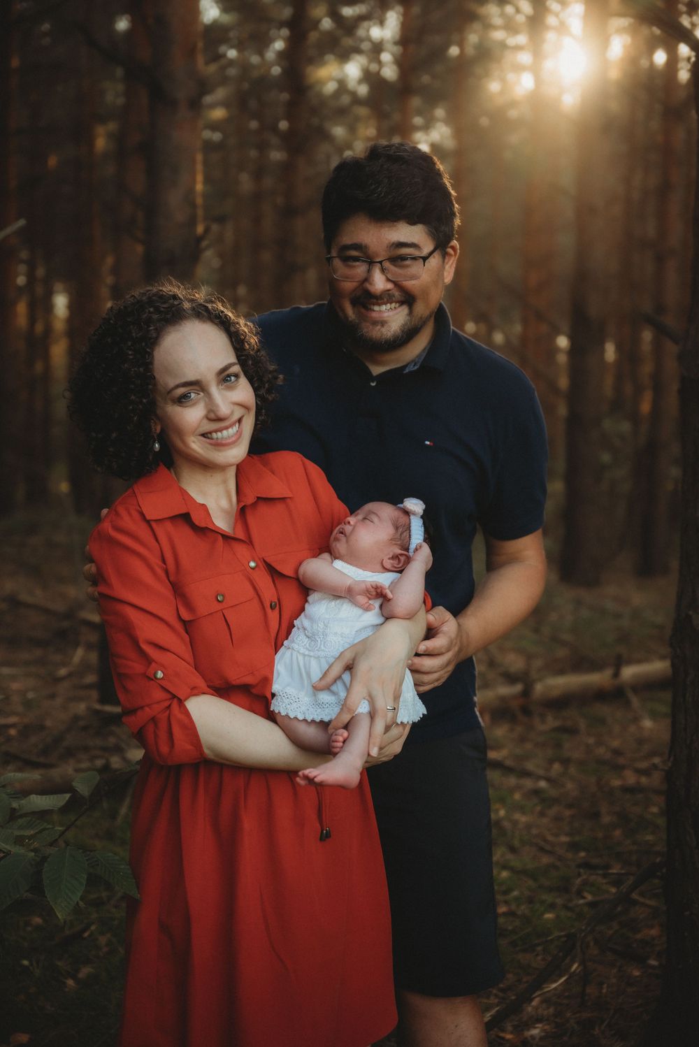 A family portrait in a sunlit forest with a newborn baby wearing white.