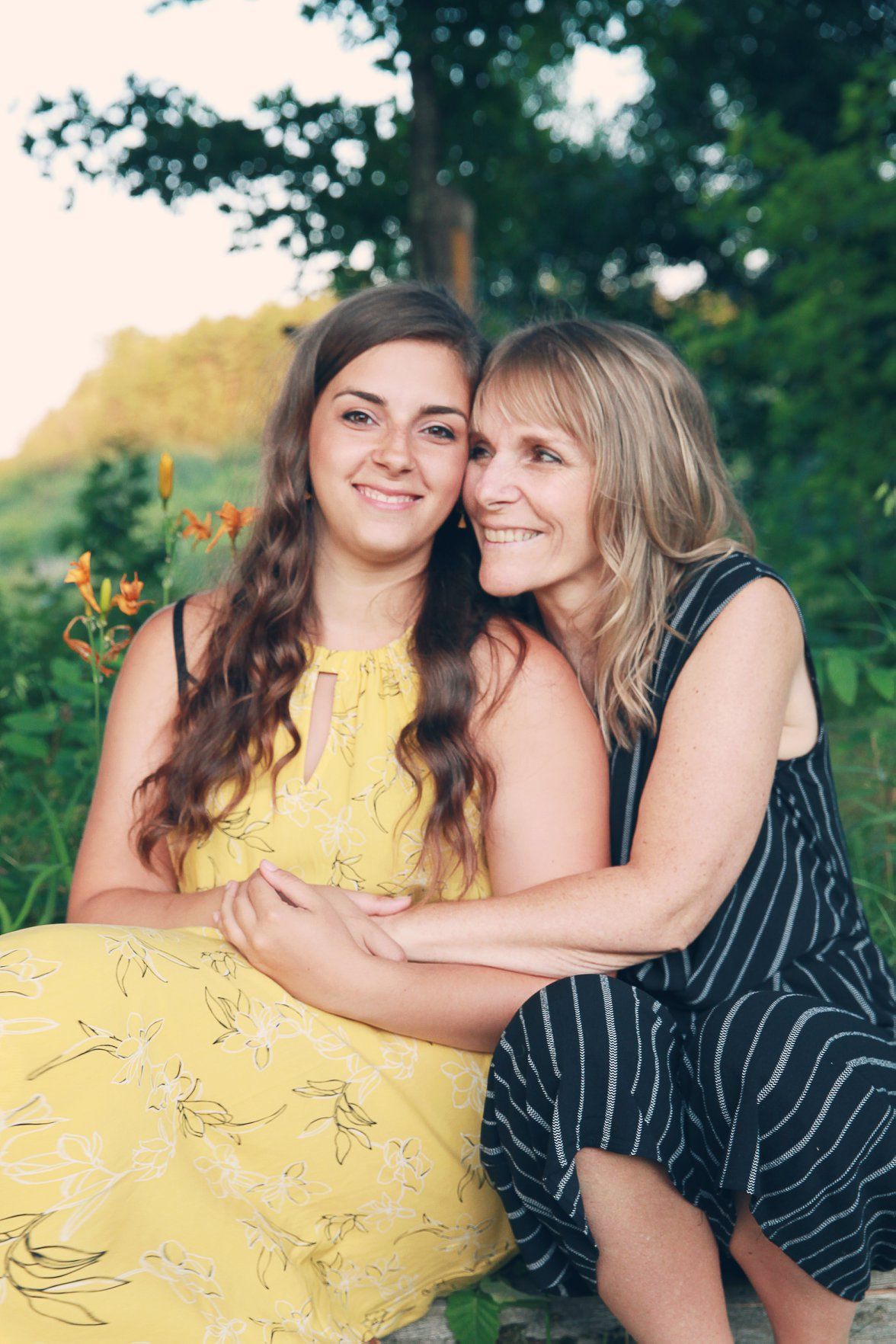 Two people embrace while wearing yellow and navy striped dresses in a summer garden setting at sunset.