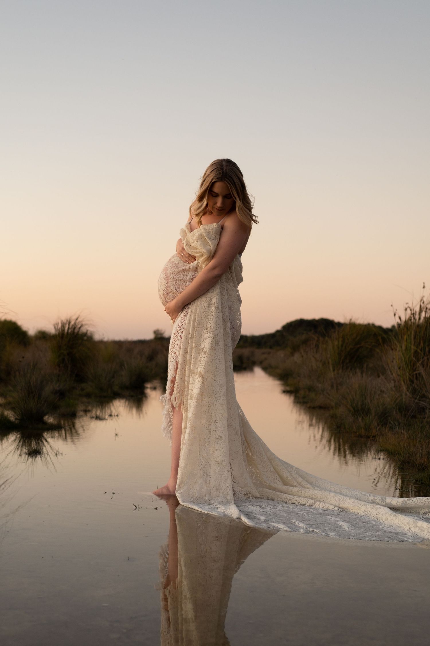 pregnant woman looking down at bump with sun setting behind her