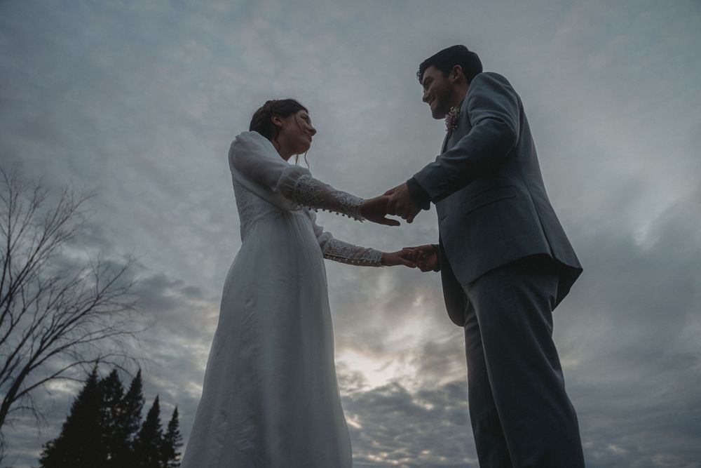 A dramatic silhouette of newlyweds holding hands against a moody evening sky.