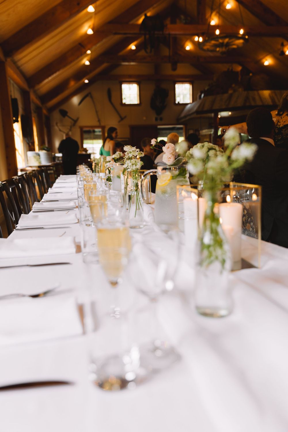 Elegant wedding reception table setting with white linens, candlelight and delicate floral centerpieces in rustic venue.