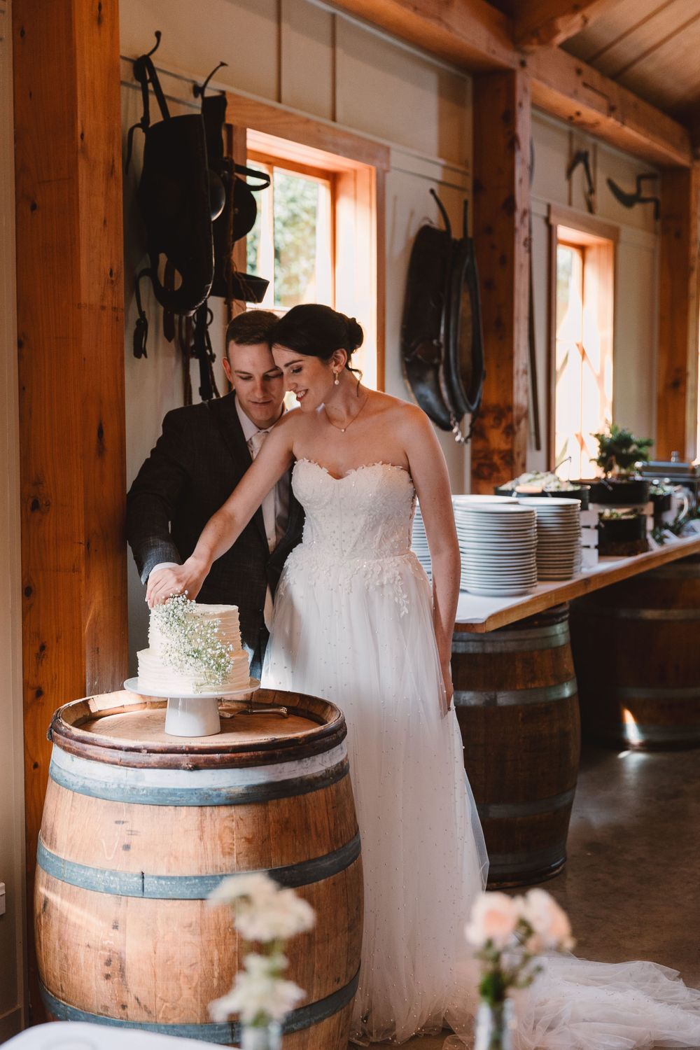 Couple cutting wedding cake displayed on rustic wine barrel.