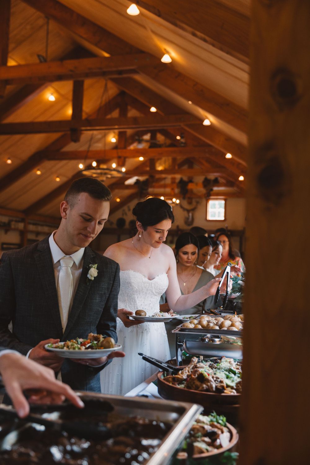 Guests serving themselves at elegant wedding buffet under wooden rafters.