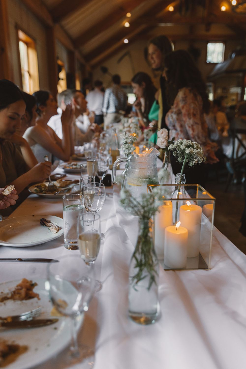 Wedding reception table set with white linens, candles and floral centerpieces in rustic venue.