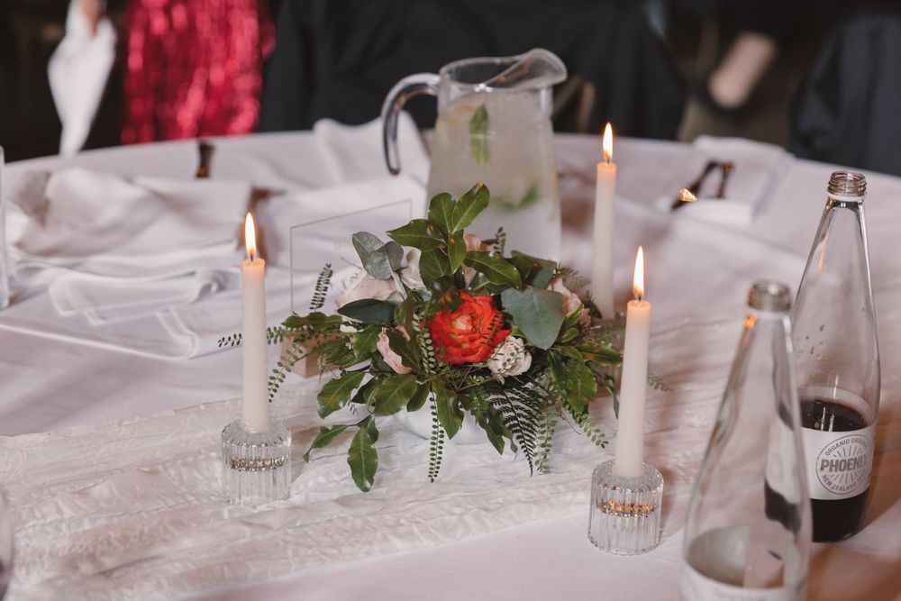 Wedding reception table with red and white floral centerpiece, candles, and glassware.