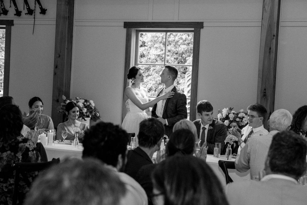 Wedding reception guests gathered in rustic venue with exposed wooden beams.