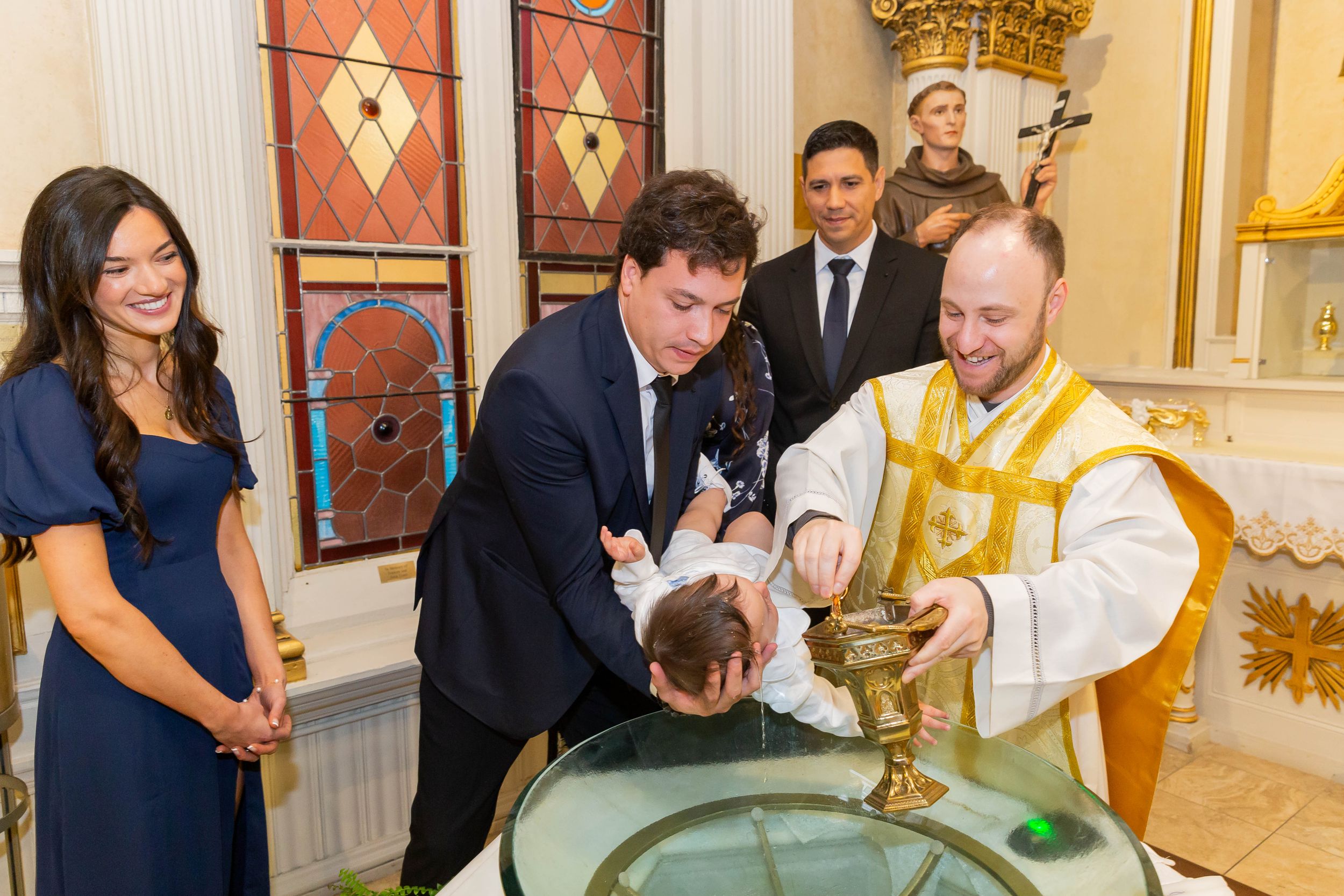 A religious baptism taking place at an ornate church font with attendees watching the ceremony.