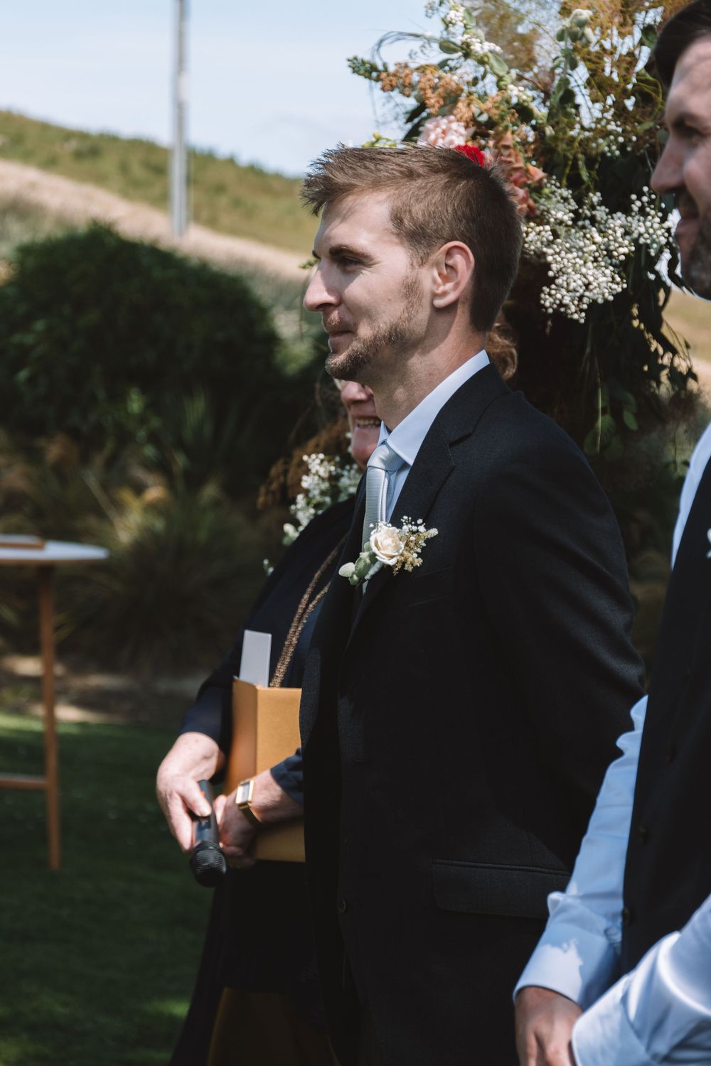 Participant in formal attire with boutonniere during outdoor wedding ceremony.