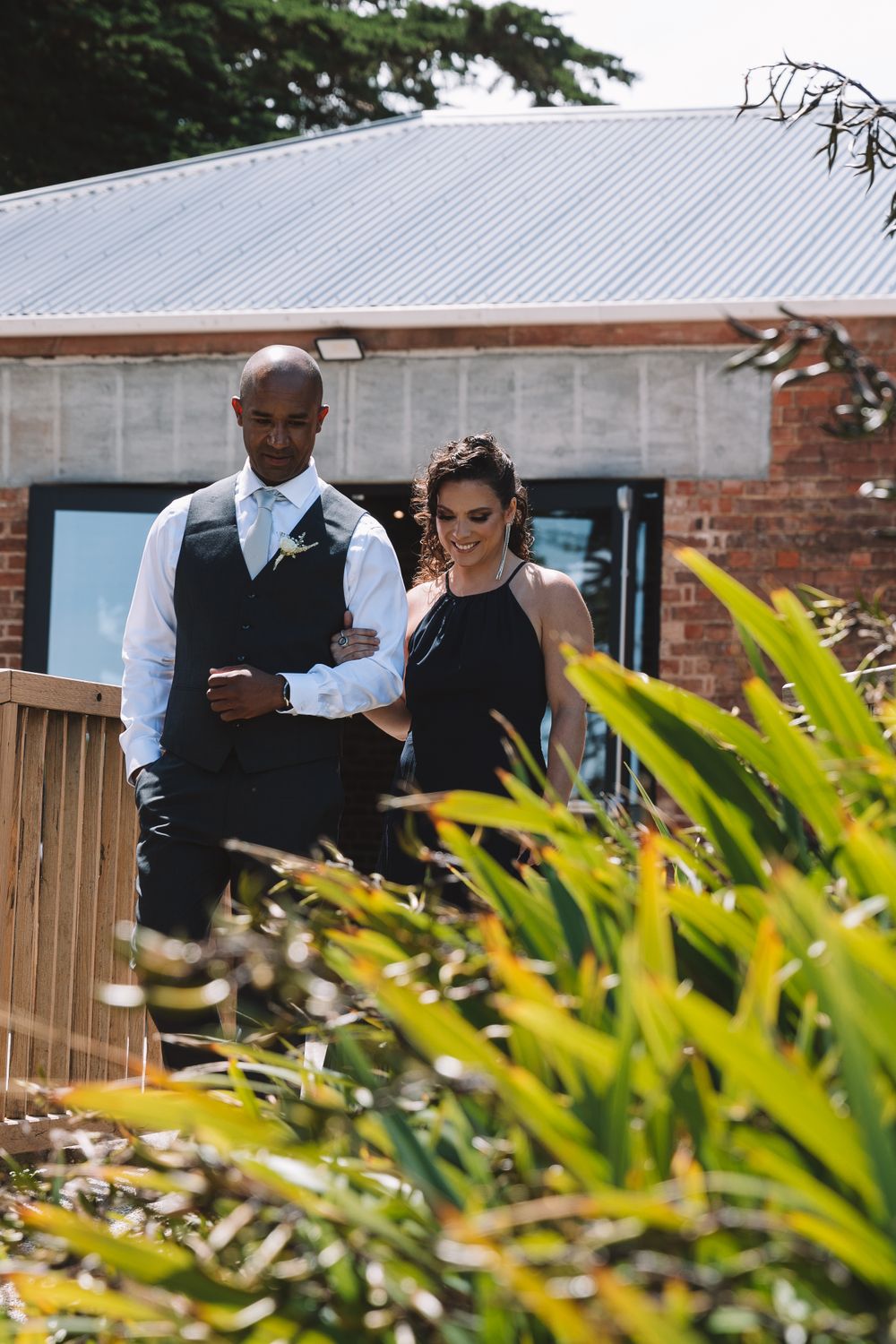 Wedding party members descend wooden deck stairs past tropical foliage.