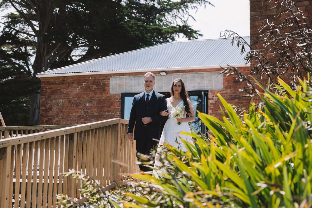 A couple stands on a wooden deck overlooking a rustic brick building surrounded by greenery.
