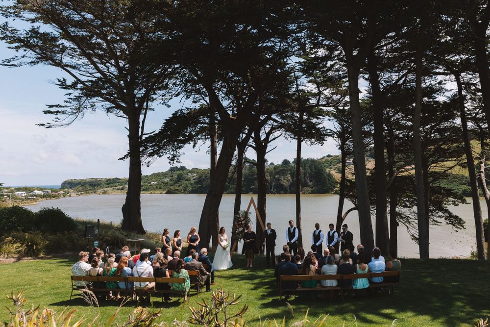 Aerial view of a lakeside wedding ceremony with guests seated under pine trees.