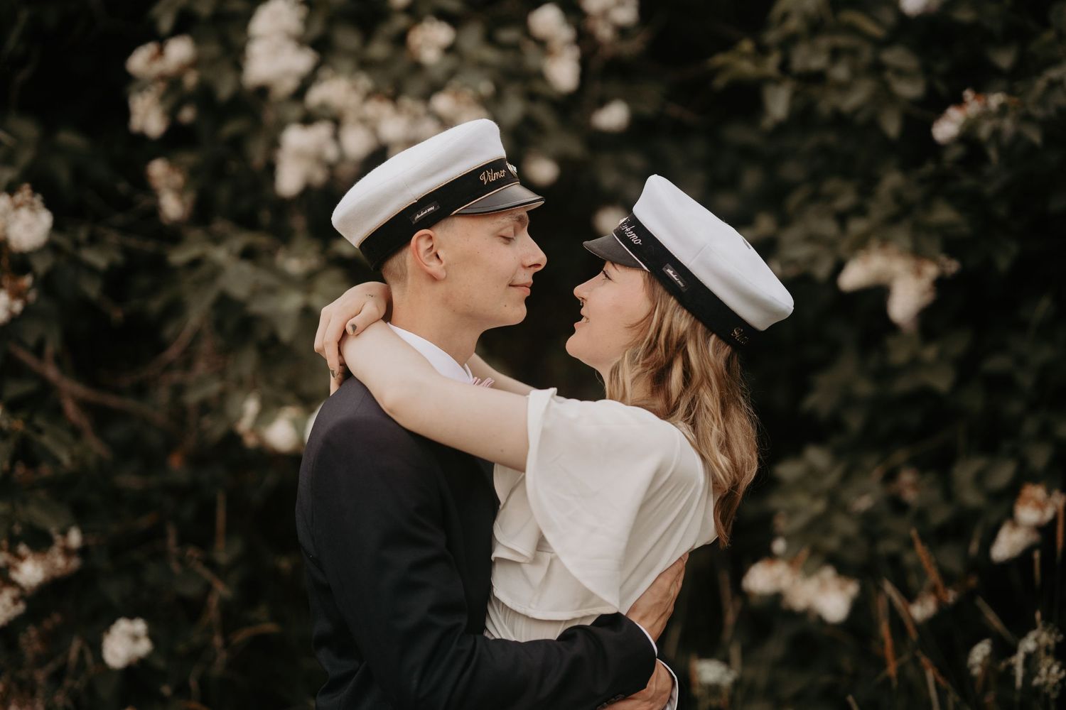 Romantic couple in nautical outfits embracing against floral backdrop.