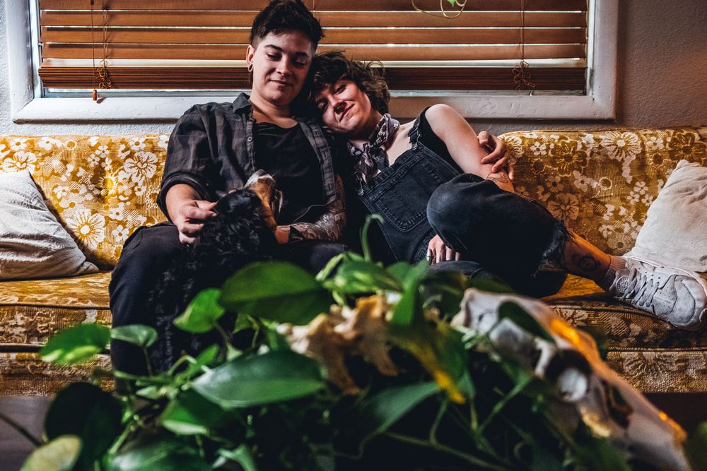 Two people relax together on a vintage floral couch with plants in the foreground.