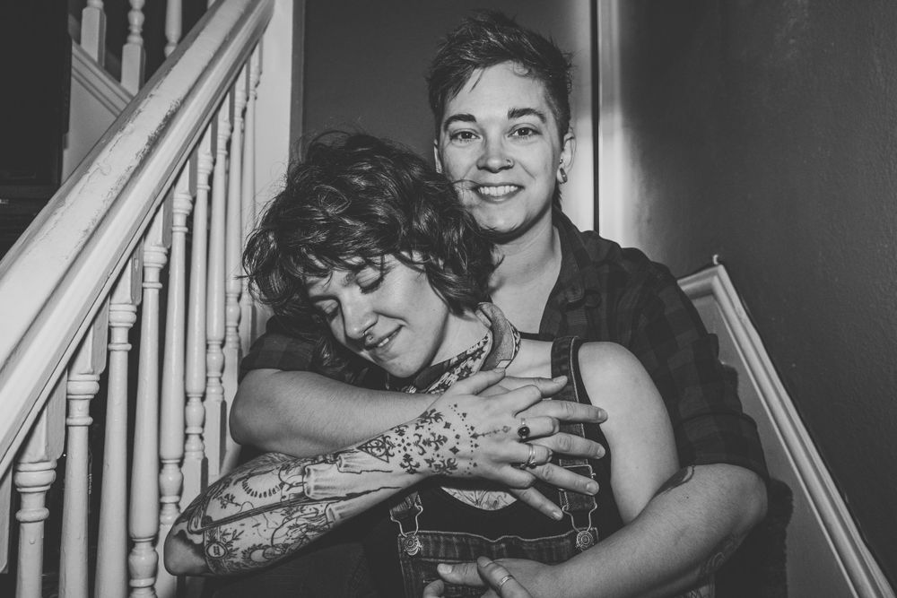 A black and white photo captures a joyful couple on stairs sharing a warm embrace.