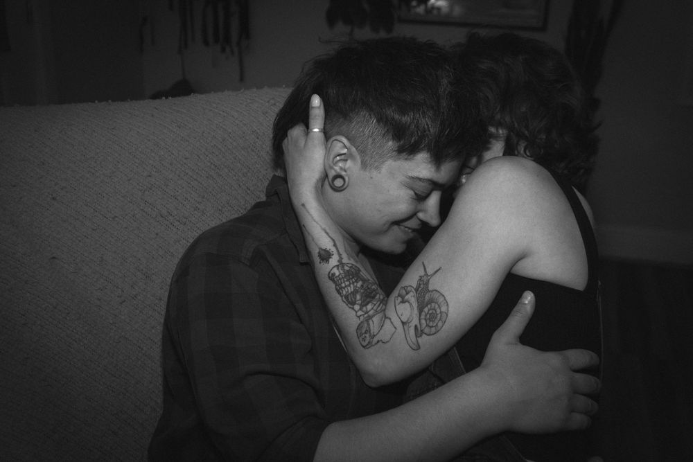 A black and white image showing a person with tattoos in an intimate, emotional moment.