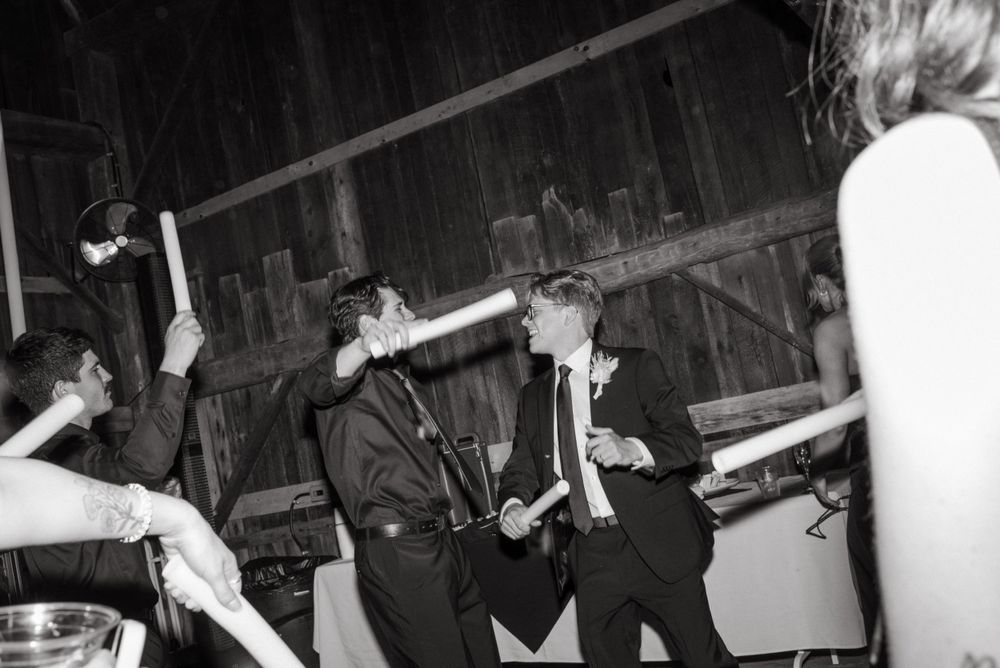 Party guests dancing enthusiastically in a rustic barn venue during a celebration in black and white.