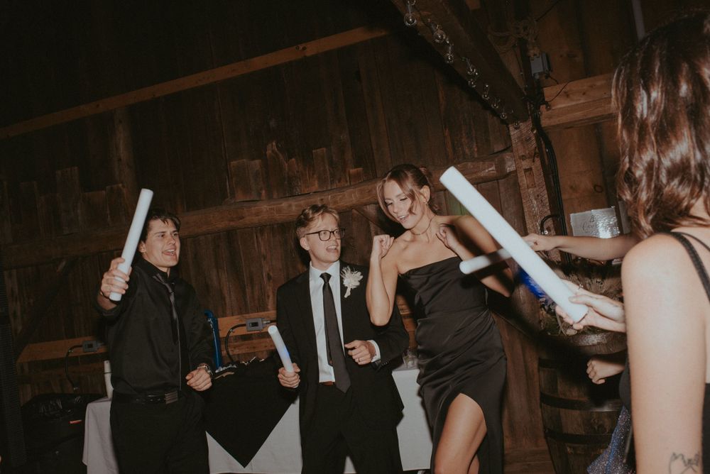 Wedding guests in black attire celebrate with illuminated foam batons at indoor reception.