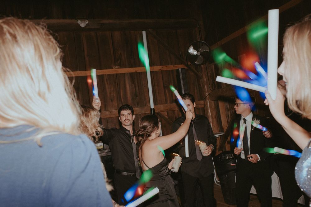 Wedding celebration in a rustic barn with guests waving colorful LED glow sticks on the dance floor.