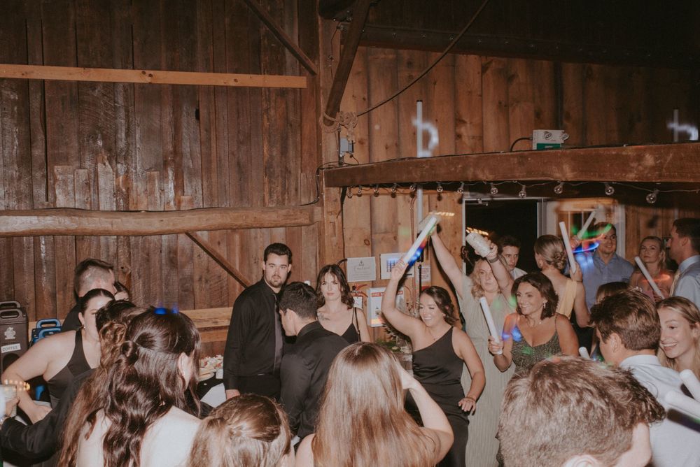 Crowd of party guests dancing with raised hands in a wooden barn during a lively celebration.