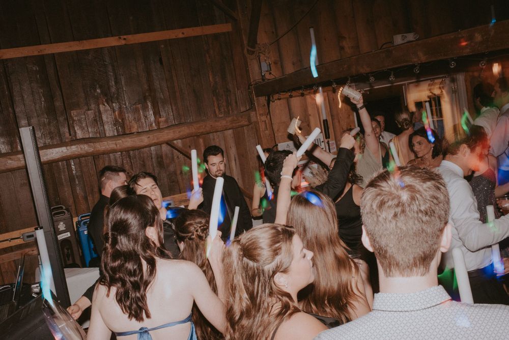Lively party scene inside a rustic barn venue with crowd dancing under blue lights.
