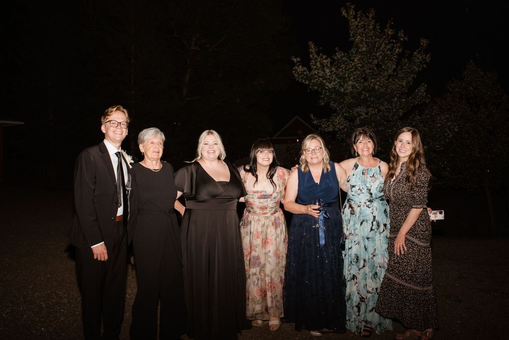 A group of seven people dressed in formal attire pose together at an outdoor nighttime gathering.
