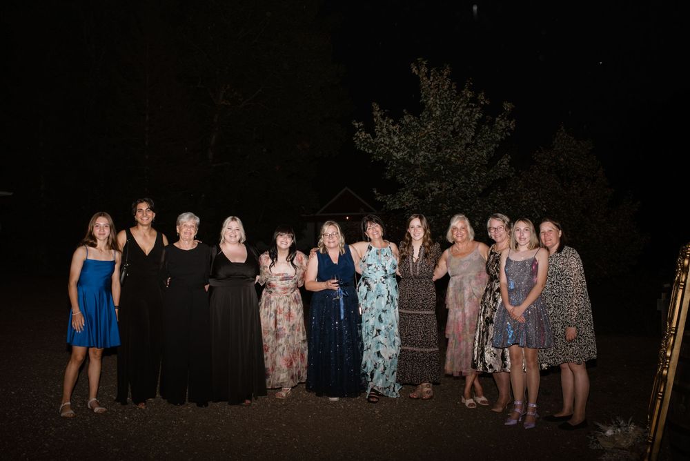 A group of people stand together outdoors at night wearing formal dresses and evening attire for a special occasion.