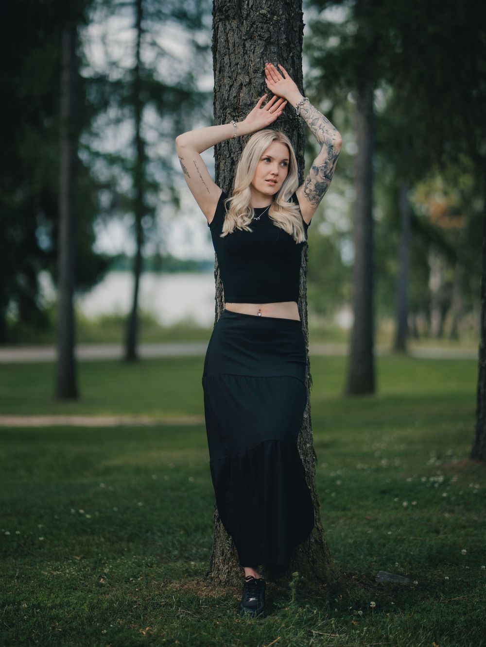 A person in dark clothing poses against a tree trunk in a misty forested park setting during golden hour.