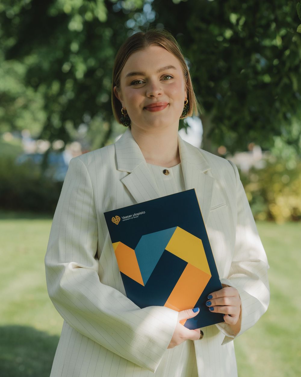 Professional wearing a crisp white blazer holds a blue folder with orange geometric design in outdoor setting.
